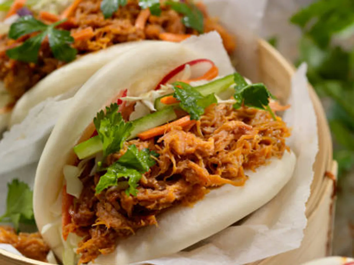 Soft steamed bao buns filled with shredded spiced pork, fresh cucumber strips, carrot, cabbage and cilantro. Served inside bamboo steamer lined with white paper.