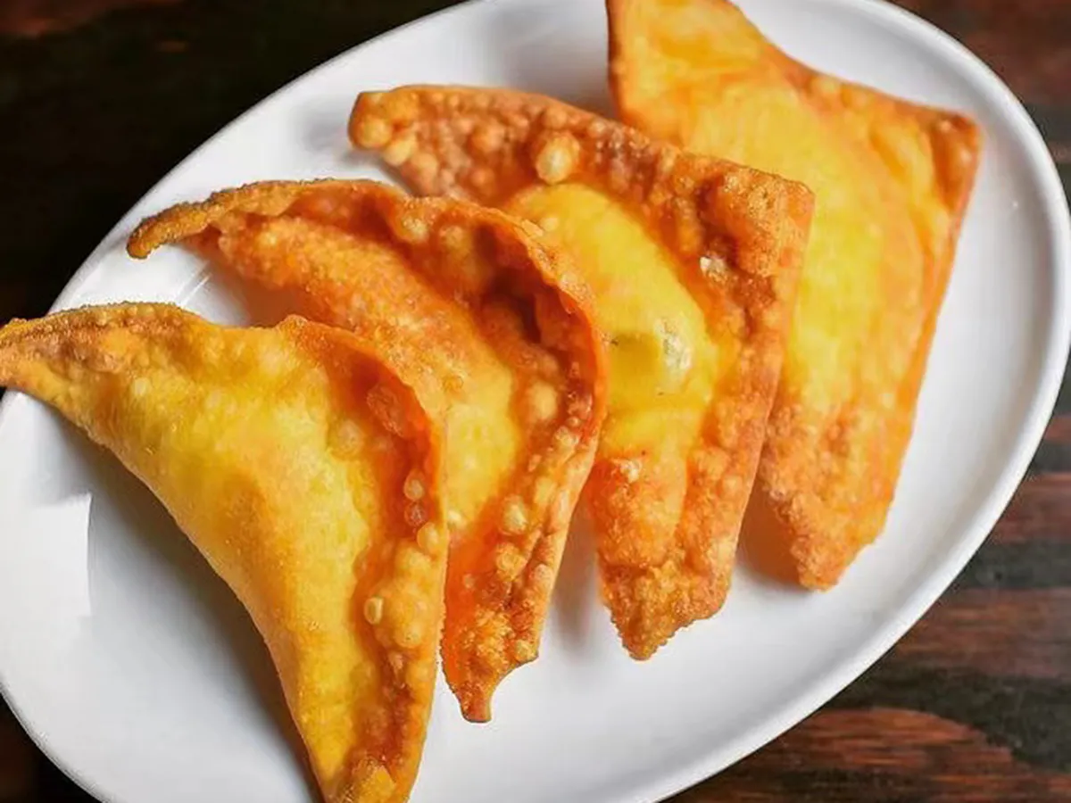 Four golden‑brown deep‑fried crispy cheese wonton triangles arranged on clean white ceramic plate, bubbly textured fried pastry crust.